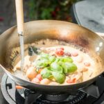 Delicious creamy tomato and basil sauce being prepared in a pan on an outdoor gas stove.