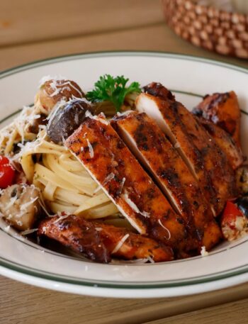 Sliced grilled chicken breast over pasta with vegetables.