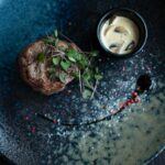 Elegant plated steak dish garnished with microgreens and served with creamy mushroom sauce.
