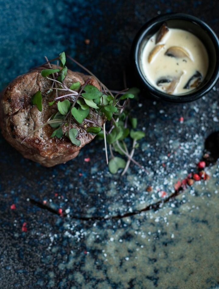 Elegant plated steak dish garnished with microgreens and served with creamy mushroom sauce.