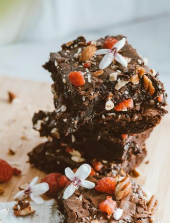 Stack of chocolate brownies garnished with nuts, berries, and flowers on a wooden board.