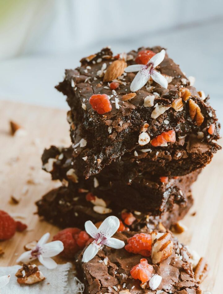 Stack of chocolate brownies garnished with nuts, berries, and flowers on a wooden board.