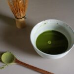 a bowl of green liquid next to a whisk