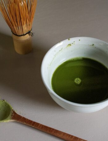 a bowl of green liquid next to a whisk
