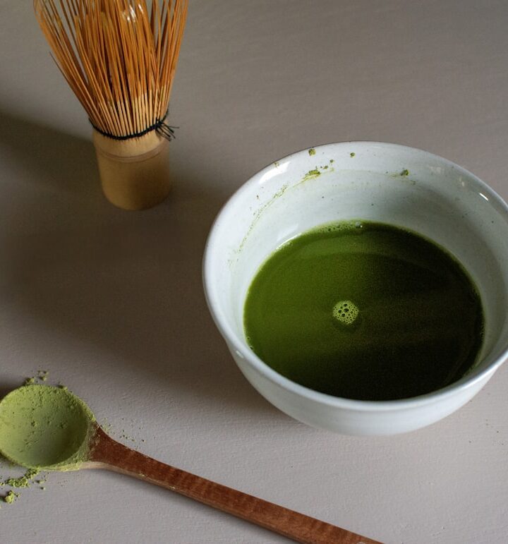 a bowl of green liquid next to a whisk