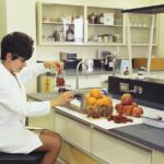 a woman in a white lab coat sitting at a counter in front of a sink