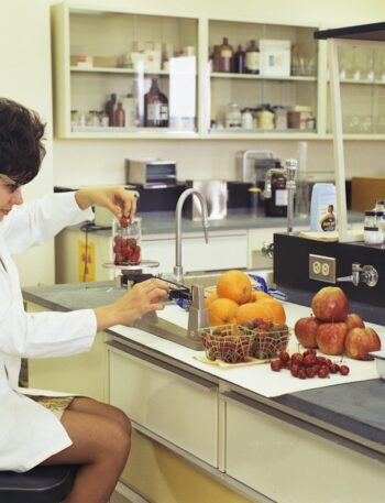 a woman in a white lab coat sitting at a counter in front of a sink